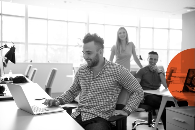 A man working at a laptop with some colleagues behind him.